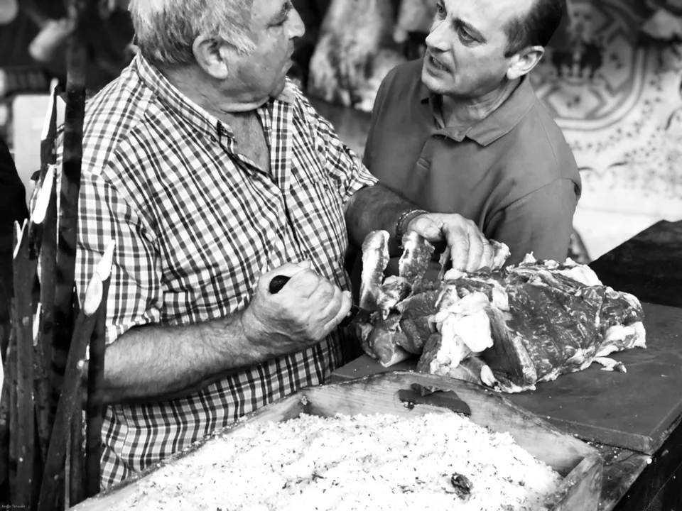 Two people talking over a market counter, photographed close up in black and white.